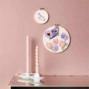 zwei gestickte runde bilder in rosa und fliedertönen an einer rosefarbenen wand. darunter ein sideboard mit zwei rosafarbenen stabkerzen