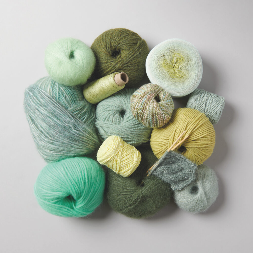 HANDSTRICK Knäuel bunter Wolle und Stricknadeln auf gelbem Hintergrund – Materialien zum Handstricken.